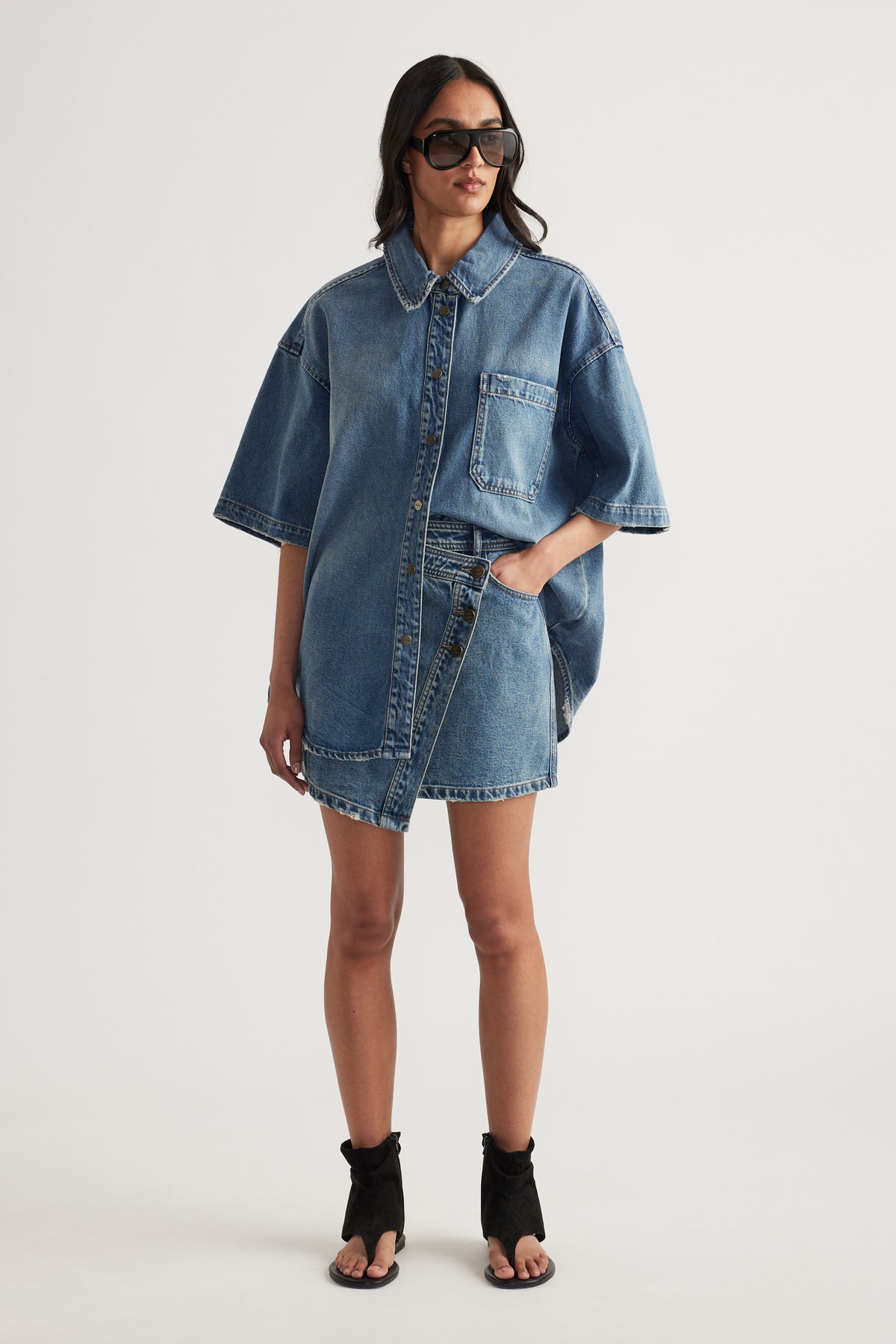 Woman wearing an oversized blue denim shirt with sunglasses and black heeled sandals