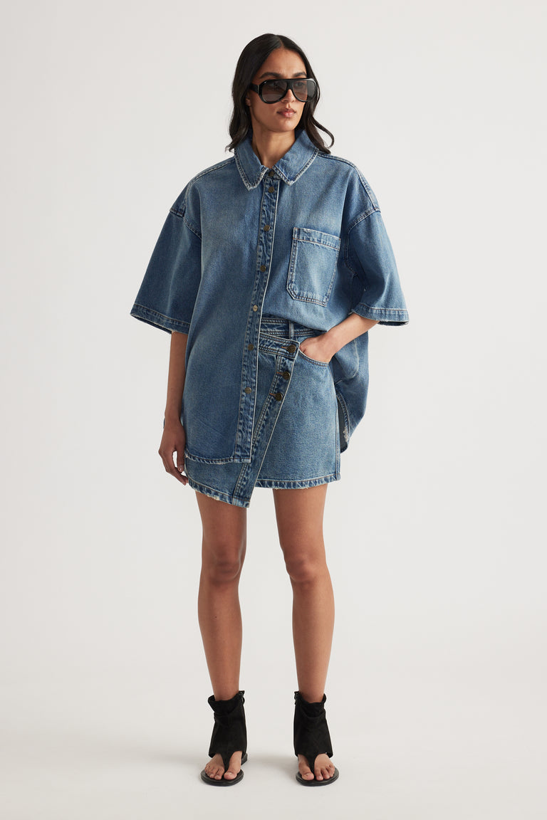 Woman wearing an oversized blue denim shirt with sunglasses and black heeled sandals