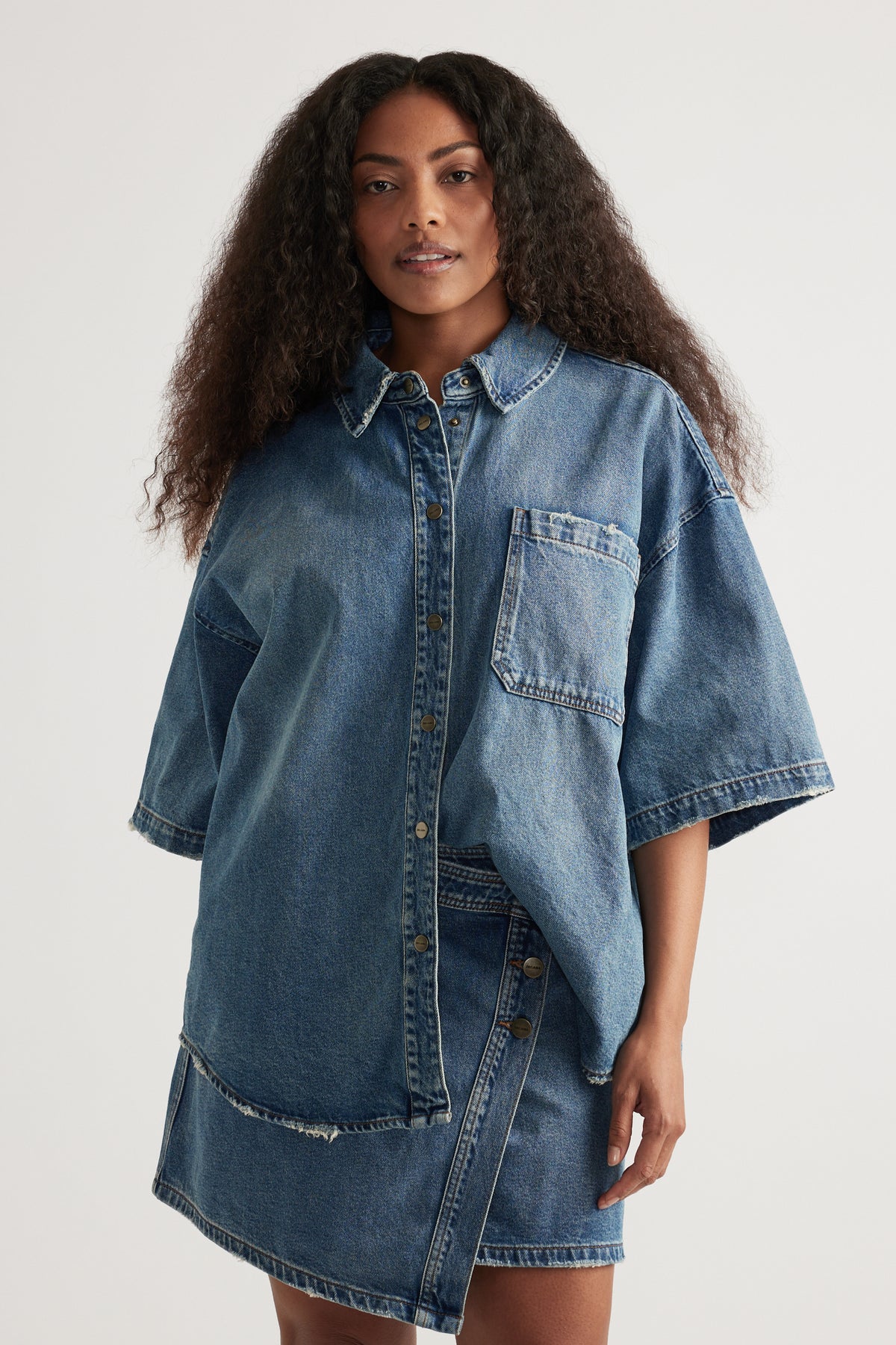 Woman wearing an oversized short sleeve denim shirt with a collared neckline and denim shorts