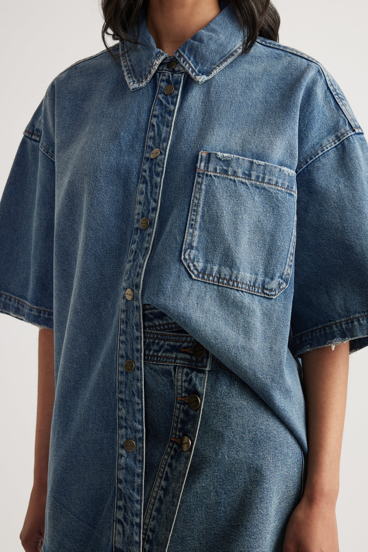 Woman wearing an oversized blue denim shirt with short sleeves, a collar and chest pocket