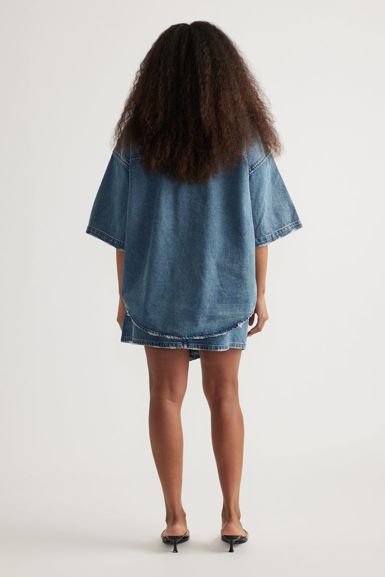 Back view of a woman wearing an oversized blue denim shirt with short sleeves and heels