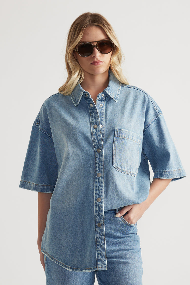 Woman wearing an oversized light blue denim shirt with short sleeves, sunglasses and matching jeans