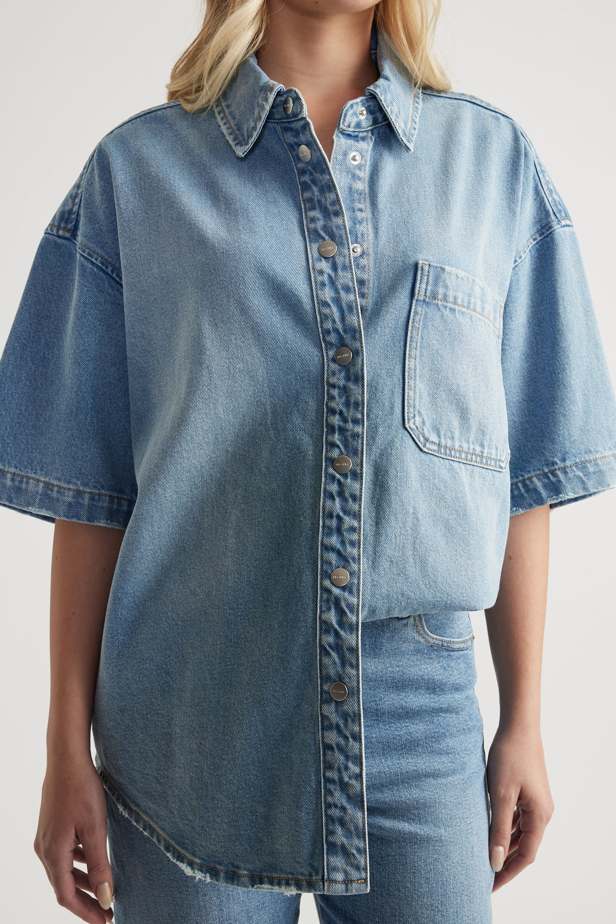 Woman wearing an oversized light wash denim shirt with short sleeves and a chest pocket
