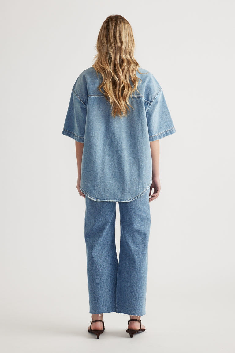 Back view of a woman wearing an oversized short sleeve denim shirt with wide leg jeans and heeled sandals