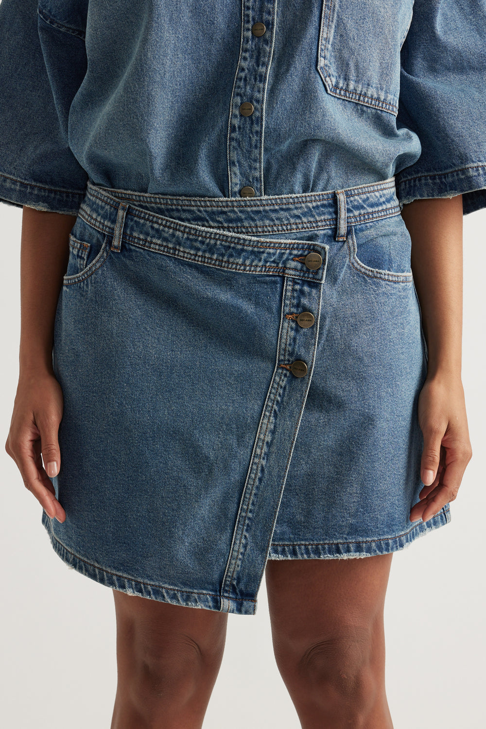 Woman wearing a high rise denim skirt with an asymmetric front and matching button up denim shirt