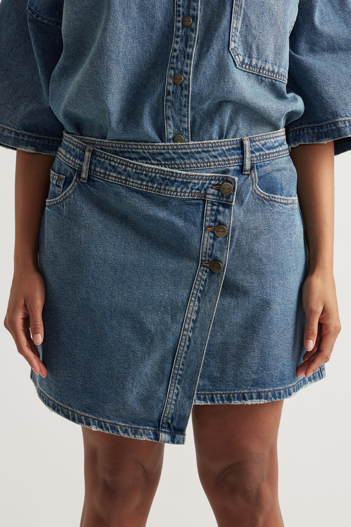 Woman wearing a high rise denim skirt with an asymmetric front and matching button up denim shirt