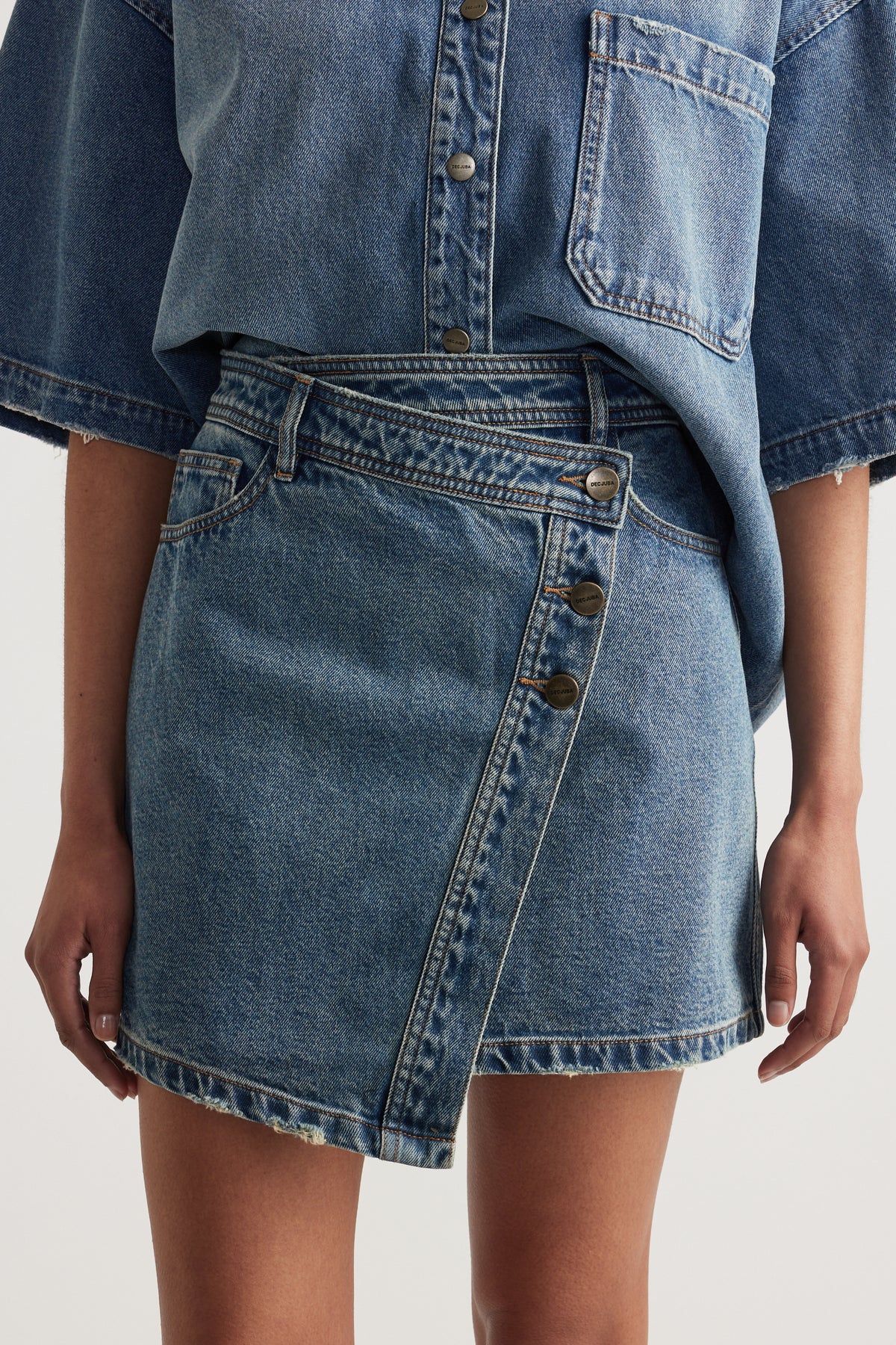 Woman wearing a blue denim shirt with chest pocket and asymmetric button front mini skirt