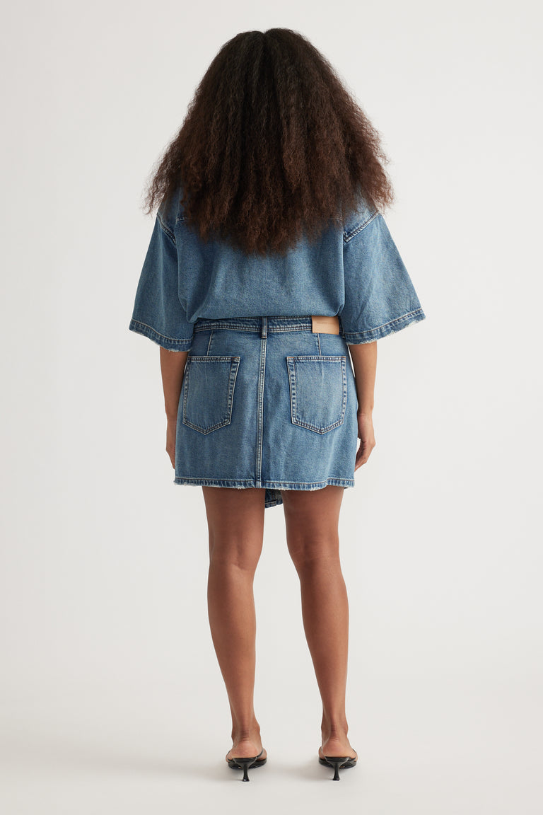 Back view of a woman wearing a denim mini skirt, cropped denim jacket and black kitten heels