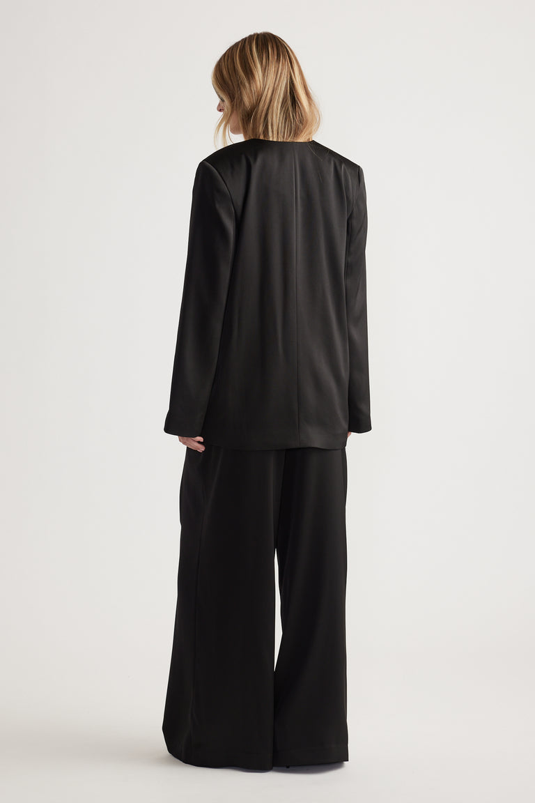 Woman with blonde hair wearing a sleek black blazer and wide-leg pants in a relaxed, elegant fit viewed from behind.