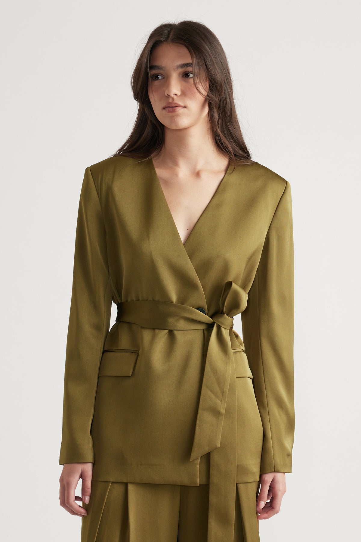 Woman wearing an olive satin blazer with a deep V-neck and a tied waist belt paired with matching wide-leg pants