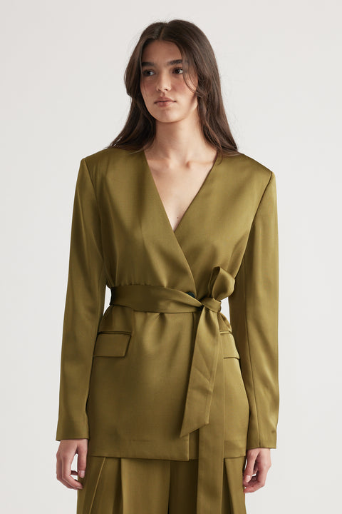 Woman wearing an olive satin blazer with a deep V-neck and a tied waist belt paired with matching wide-leg pants