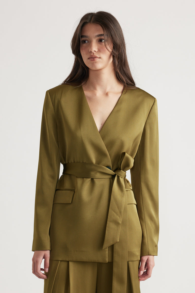 Woman wearing an olive satin blazer with a deep V-neck and a tied waist belt paired with matching wide-leg pants