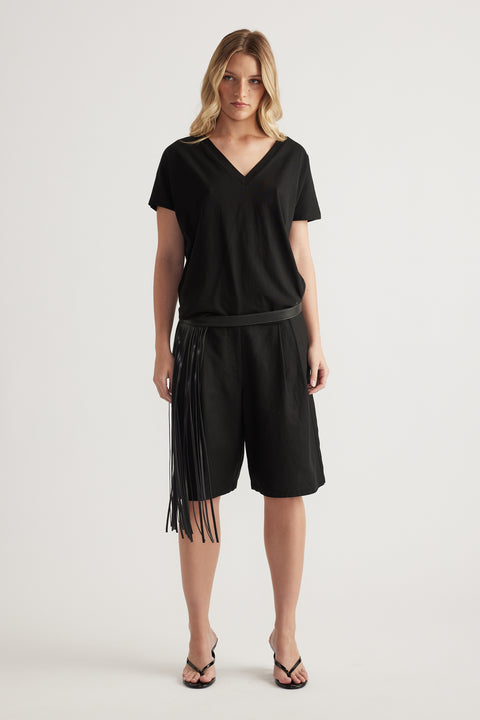 Woman wearing a black boxy V neck tee with black fringe shorts and flat sandals