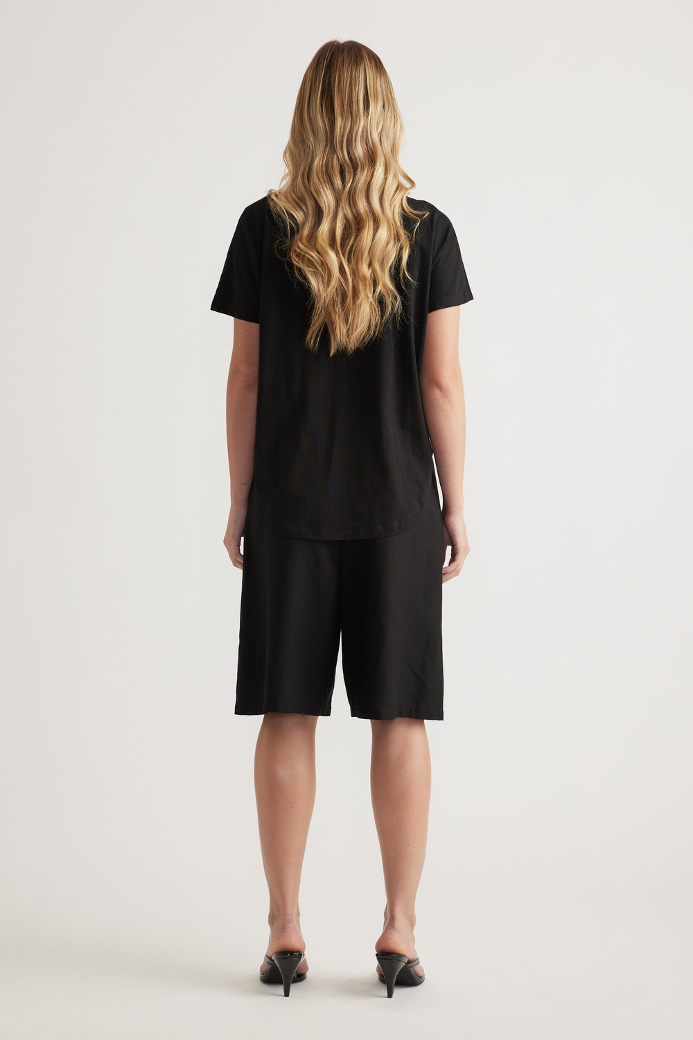 Back view of a woman wearing a black boxy tee with black knee-length shorts and heels
