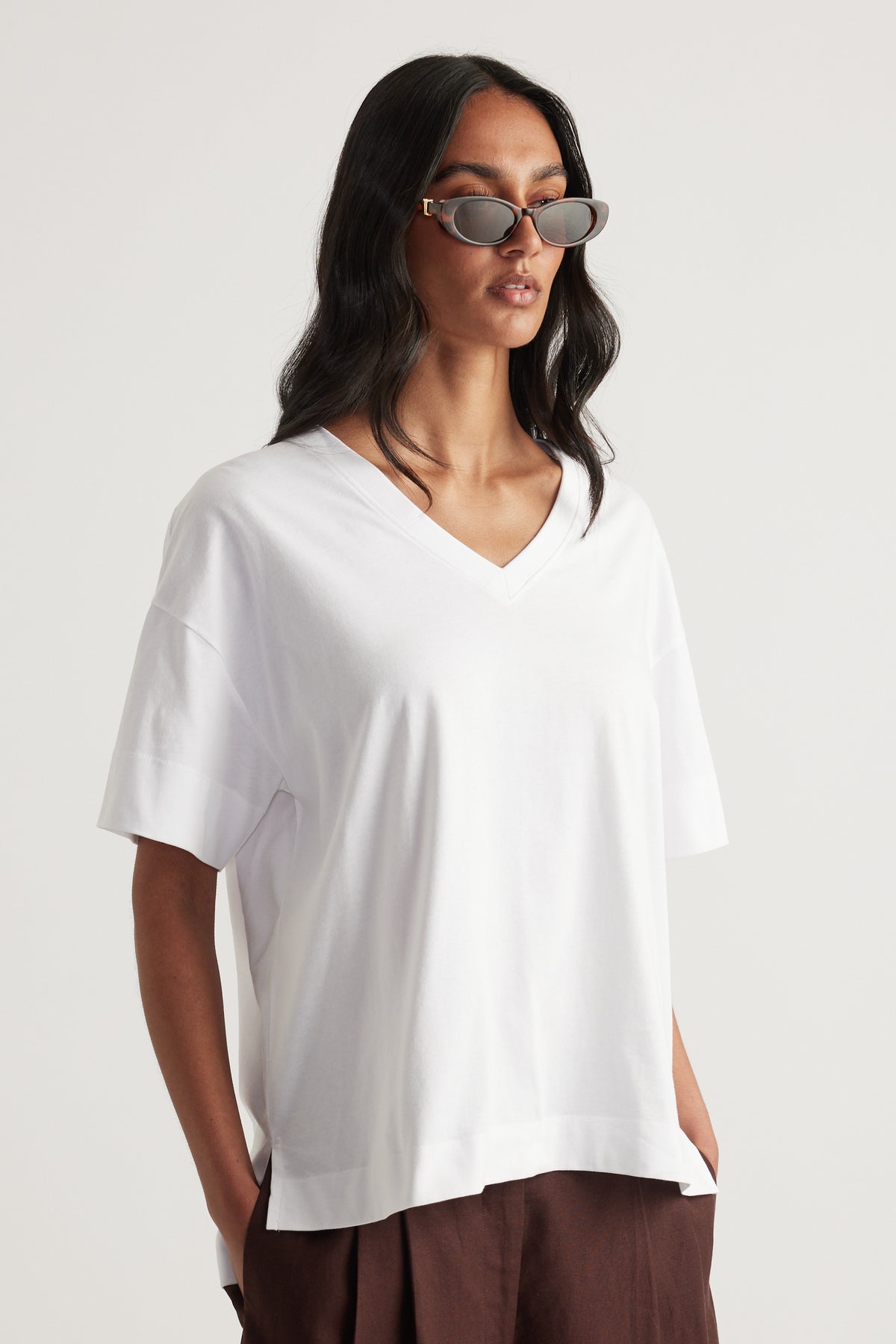 Woman wearing a white boxy V neck tee with brown pants and sunglasses