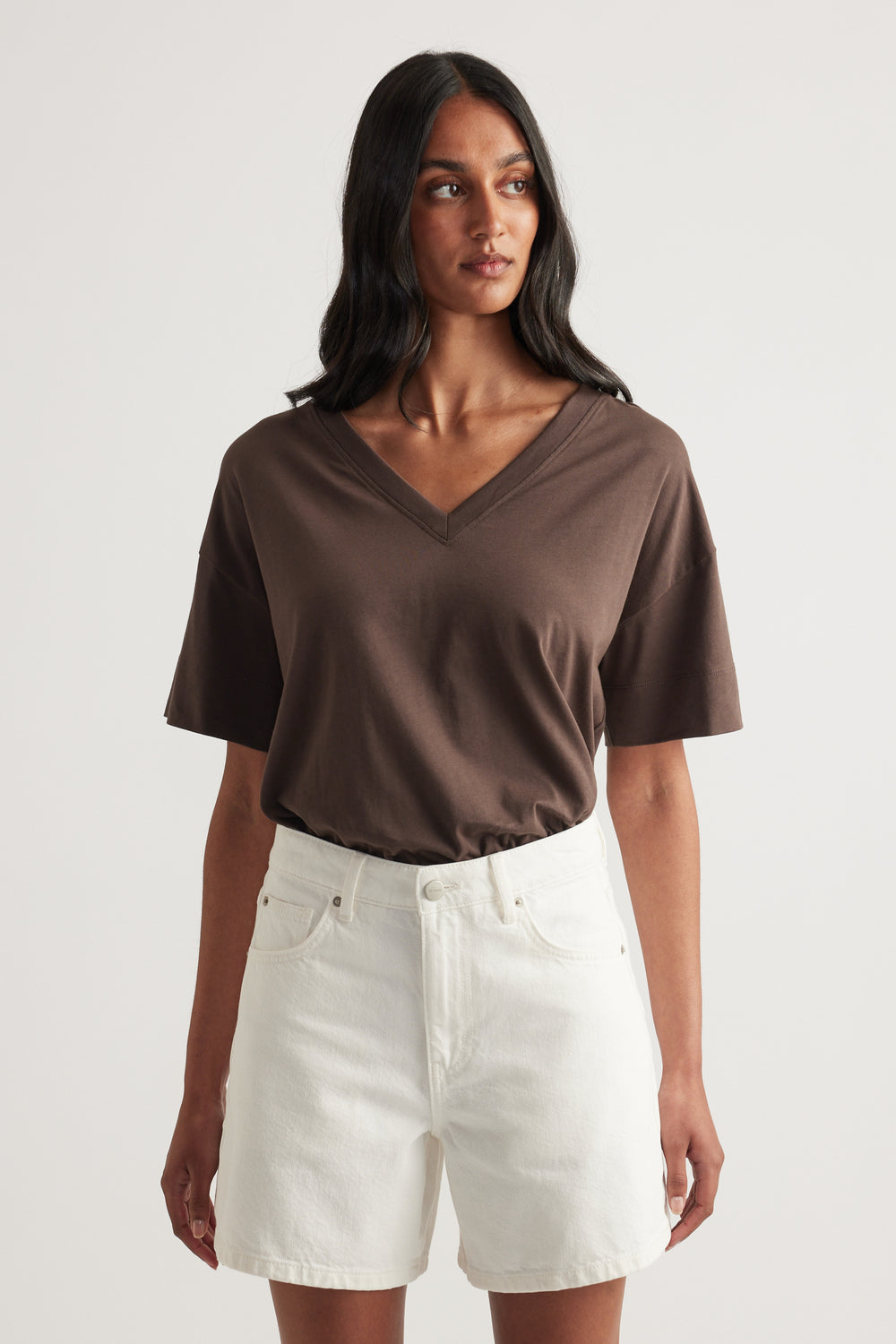 Woman wearing a brown boxy V neck tee with white denim shorts