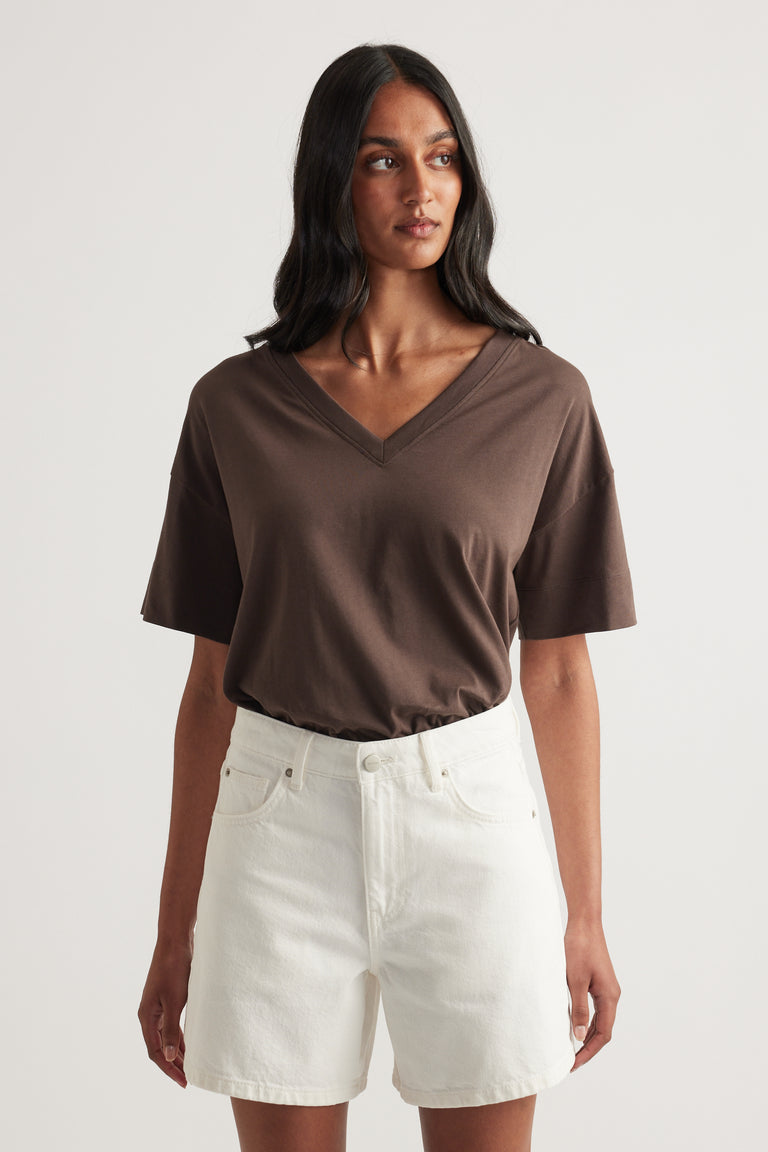 Woman wearing a brown boxy V neck tee with white denim shorts