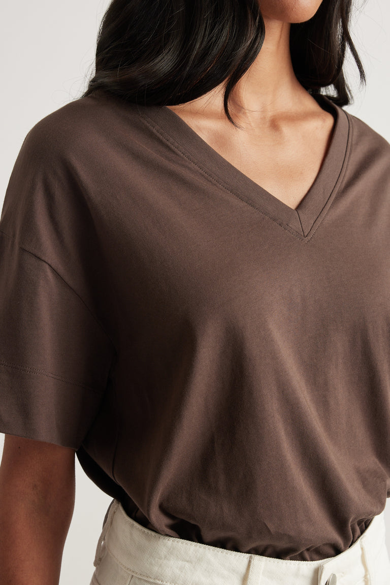 Woman wearing a brown boxy V neck tee tucked into off white pants