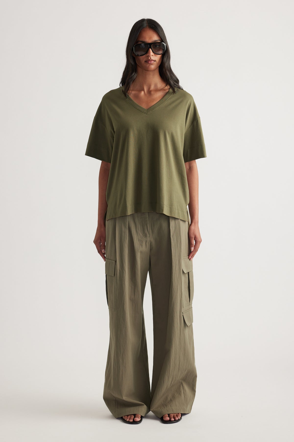 Woman wearing an olive green boxy V neck tee with relaxed cargo pants and black sunglasses