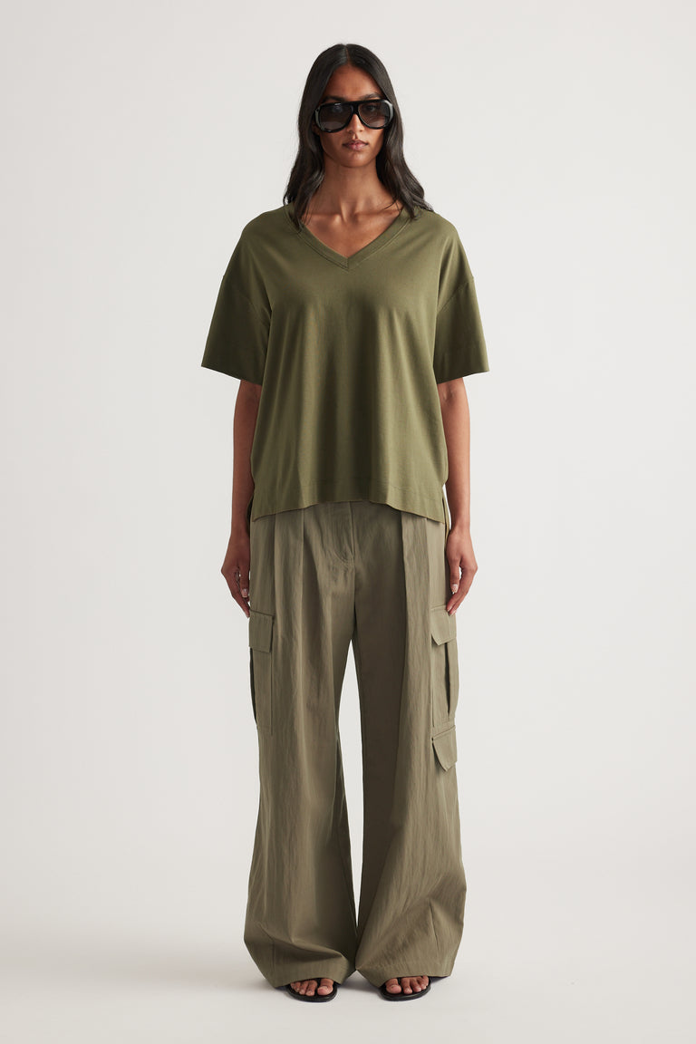 Woman wearing an olive green boxy V neck tee with relaxed cargo pants and black sunglasses