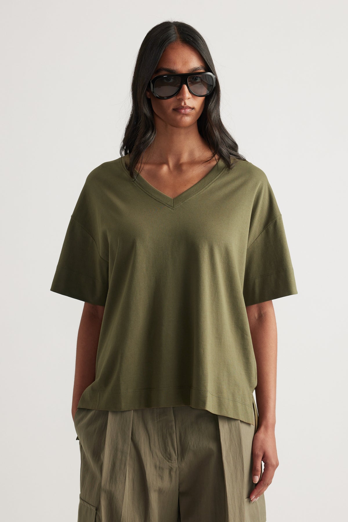 Woman wearing an olive green boxy V-neck tee with relaxed sleeves and wide-leg pants