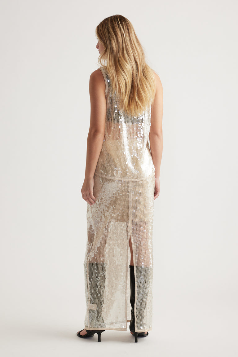 Woman wearing a sleeveless shimmering sequin tank and matching long skirt with side slit in soft neutral tones