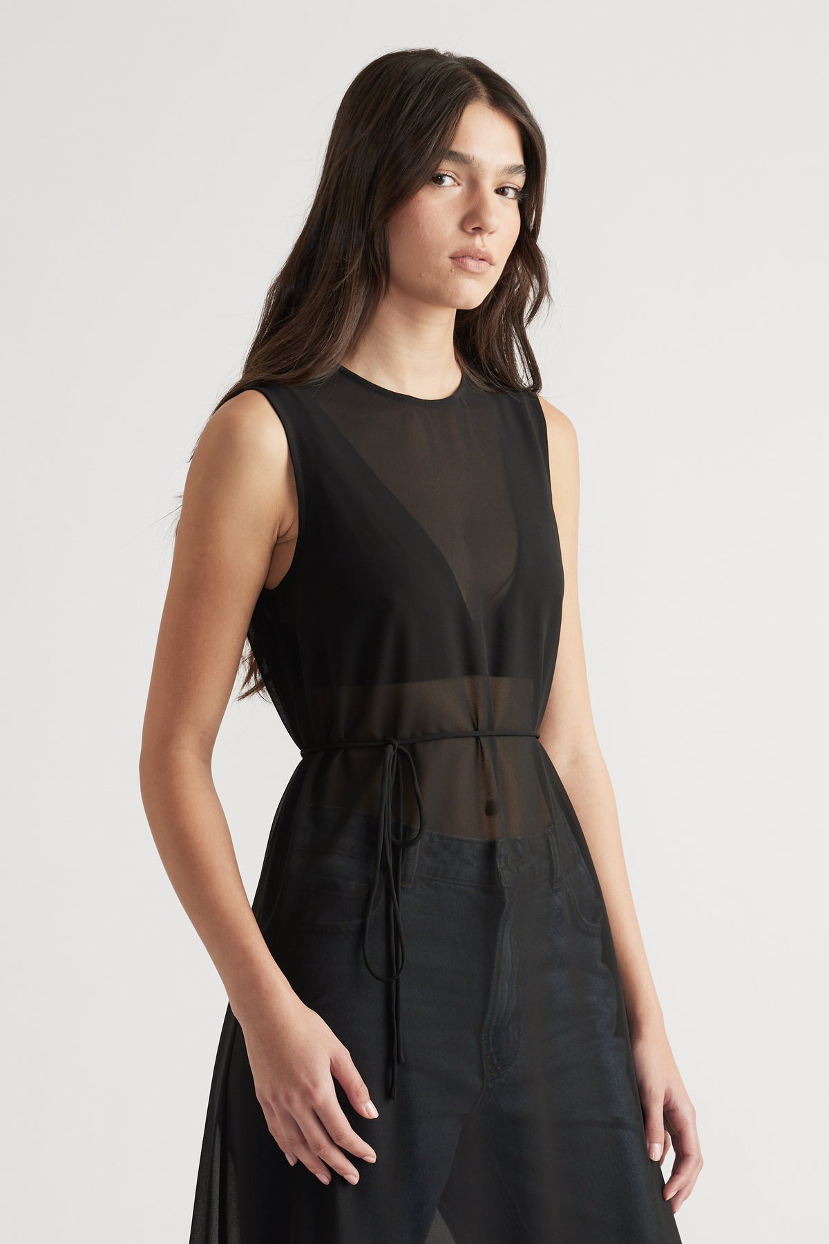 Woman wearing a sleeveless black sheer maxi dress with a cinched waist, styled for an elegant and modern look