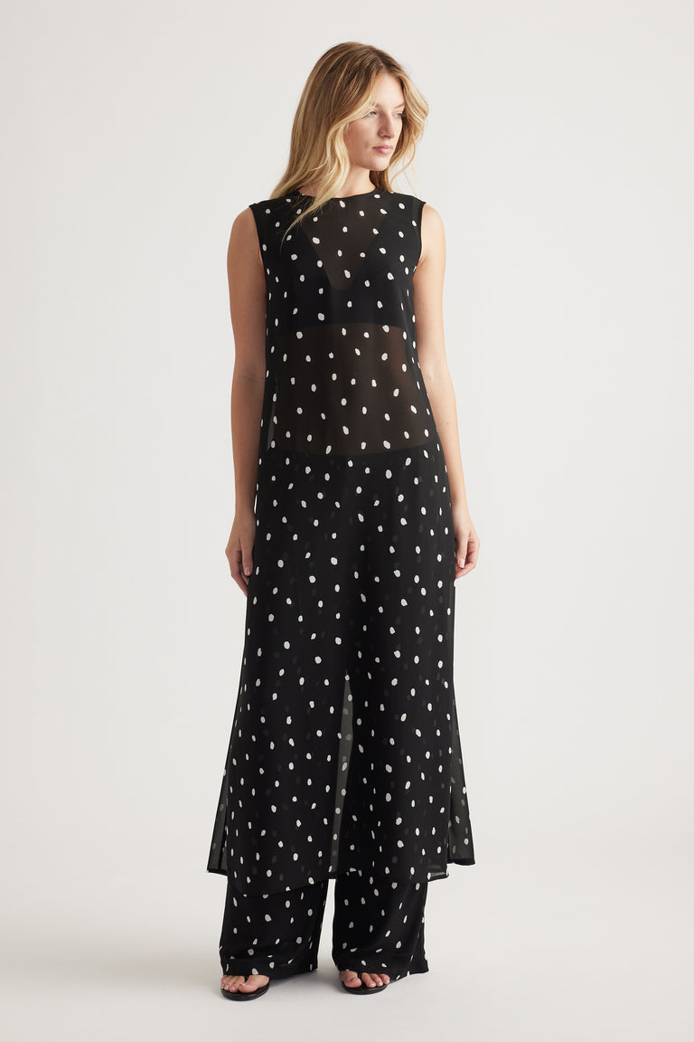 Woman wearing a sleeveless black maxi dress with white polka dots and sheer paneling layered over matching wide-leg pants