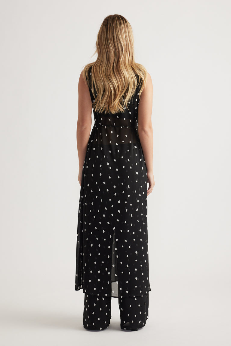 Woman wearing a black sheer maxi dress with white polka dots layered over matching wide-leg pants, back view