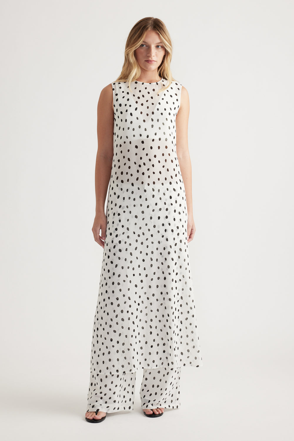 Woman wearing a sleeveless white maxi dress with irregular black spots and matching wide-leg pants for a relaxed look