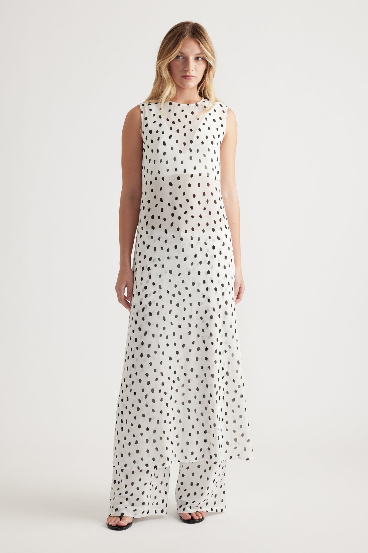 Woman wearing a sleeveless white maxi dress with irregular black spots and matching wide-leg pants for a relaxed look