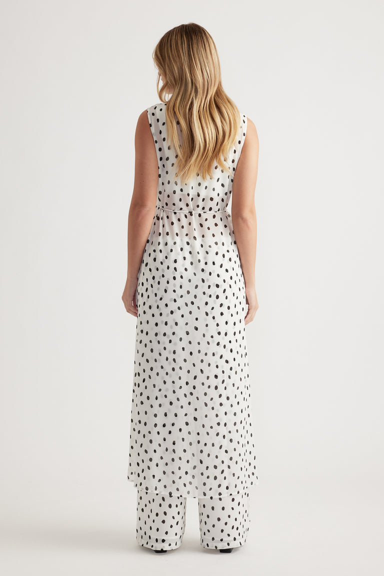 Woman wearing a sleeveless white maxi dress with black polka dots, paired with matching wide-leg trousers, back view