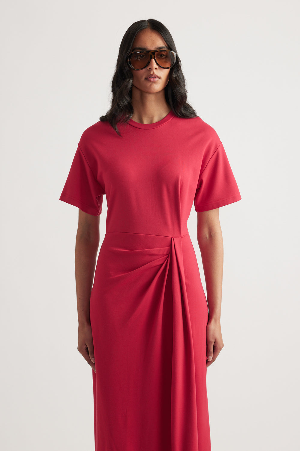 Woman wearing a red short sleeve midi dress with a round neck and gathered waist knot detail
