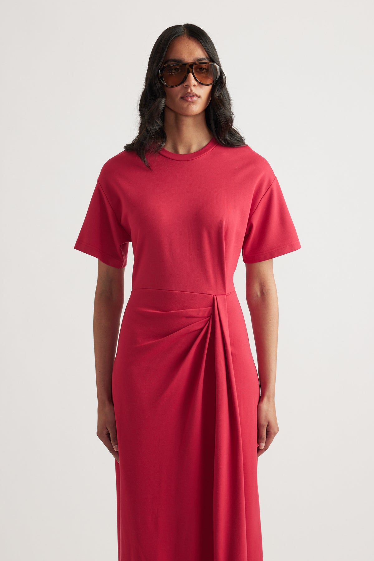 Woman wearing a red short sleeve midi dress with a round neck and gathered waist knot detail