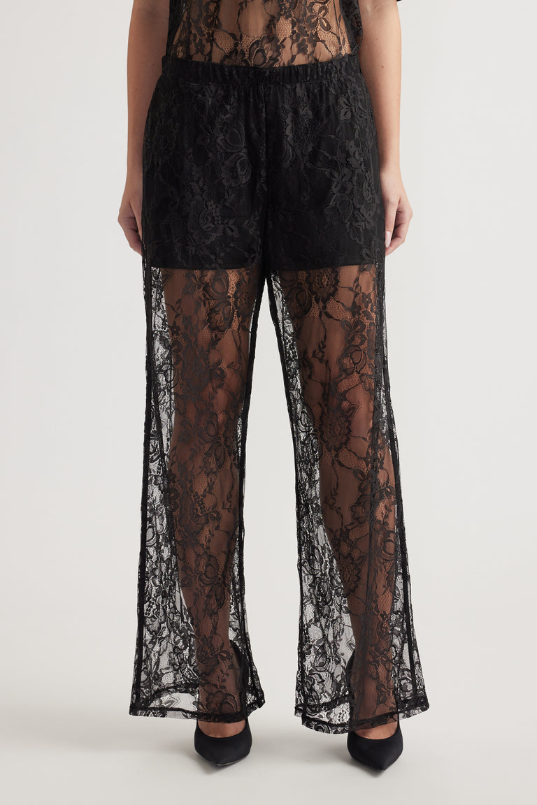 Black wide-leg lace pants with elastic waist and detachable lining worn with black heels on neutral background
