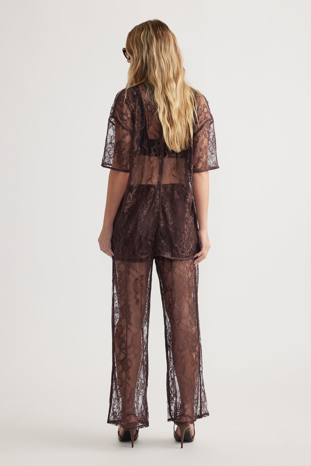 Woman seen from back wearing sheer lace pant and matching loose lace top with short sleeves and high heels