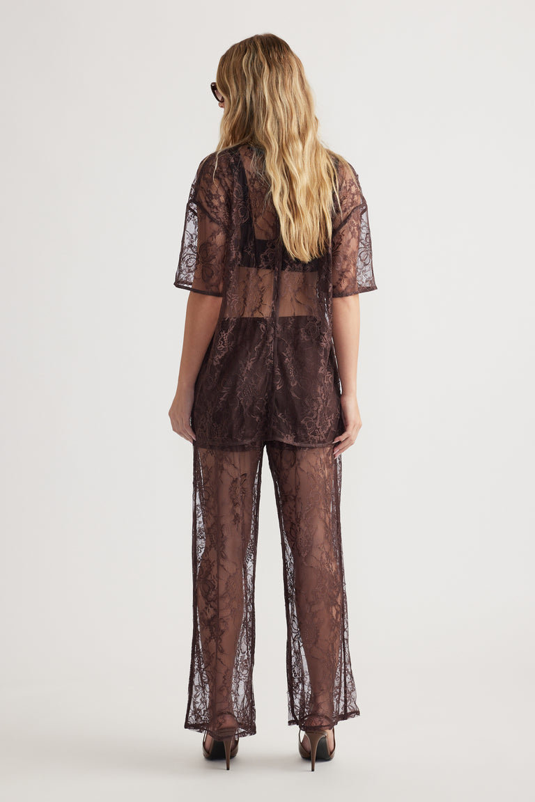 Woman seen from back wearing sheer lace pant and matching loose lace top with short sleeves and high heels