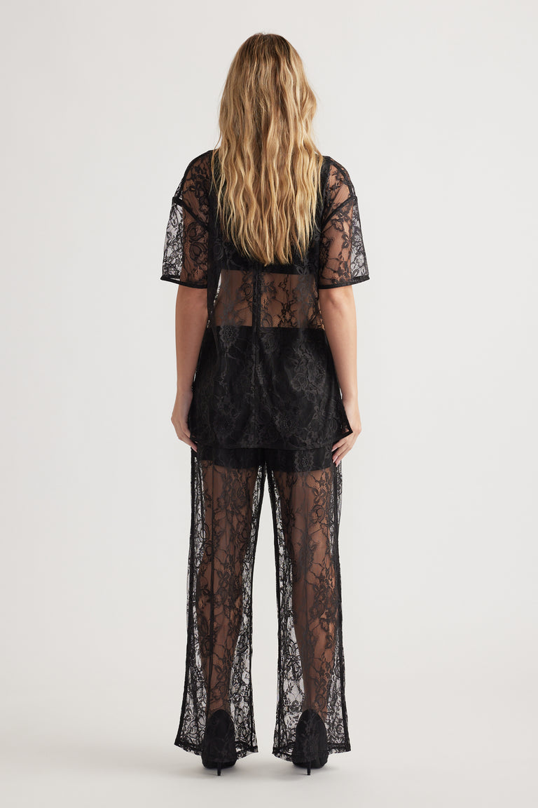 Rear view of woman wearing sheer black lace top and matching lace pants with black underlayer and heels