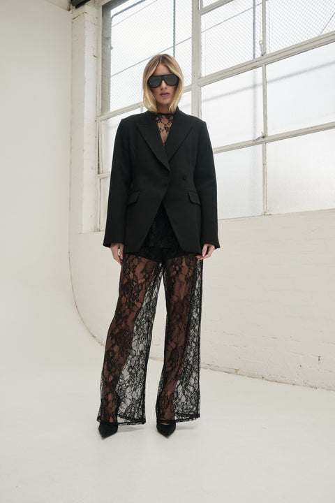 Woman wearing black lace wide leg pants with a tailored blazer, sunglasses and pointed heels