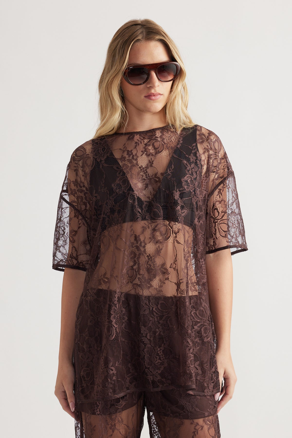 Woman wearing sheer floral lace top with short sleeves styled over black innerwear and matching lace bottoms