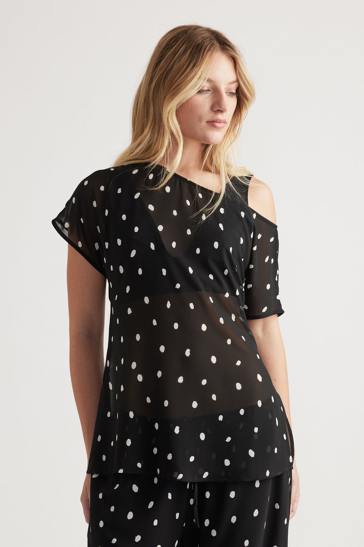 Woman wearing a black sheer top with white polka dots and an off-shoulder detail, styled with matching pants