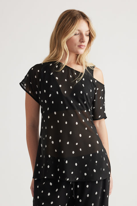 Woman wearing a black sheer top with white polka dots and an off-shoulder detail, styled with matching pants