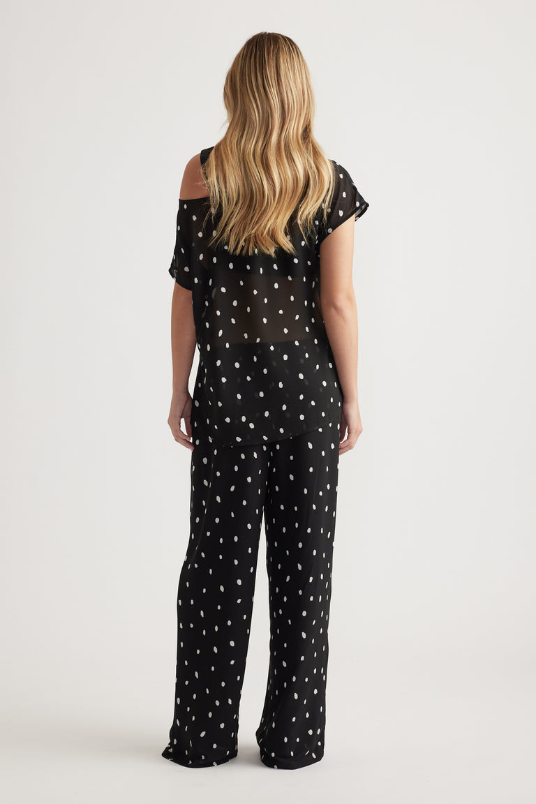 Woman seen from behind wearing a black sheer off-shoulder top with white spots paired with matching loose pants