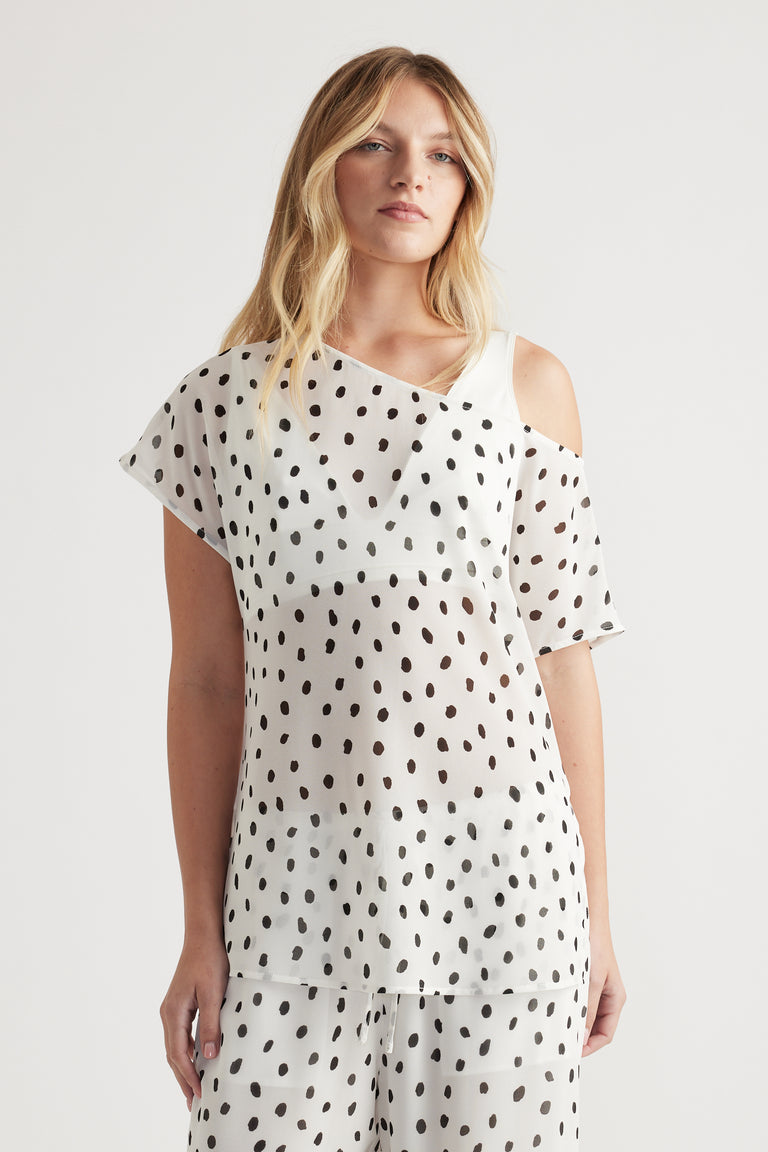 Woman wearing a white sheer top with black polka dots and an off-shoulder design paired with matching patterned pants