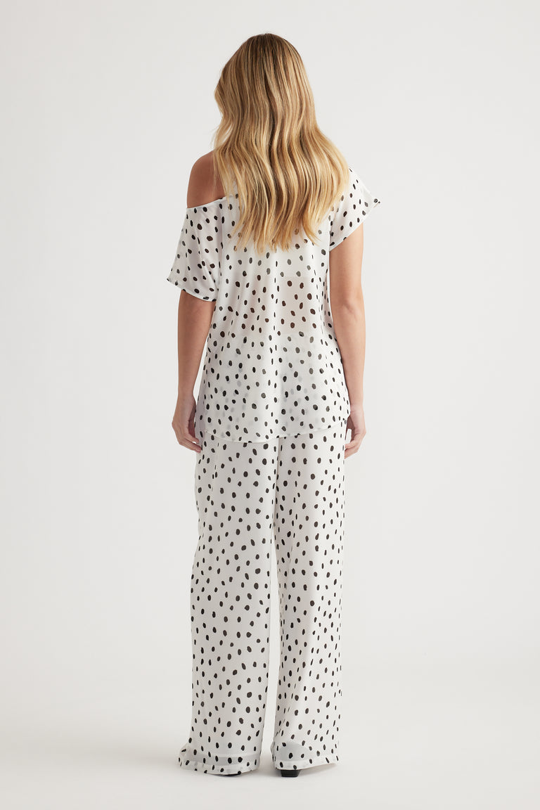 Woman wearing a lightweight off-shoulder white top with black irregular dots paired with matching wide-leg pants from behind