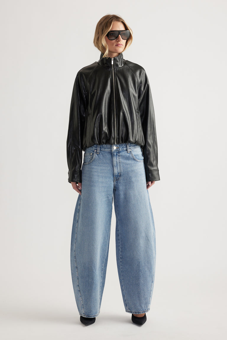 Woman wearing a black faux leather bomber jacket with zipper and wide-leg light blue denim jeans and black pointed shoes