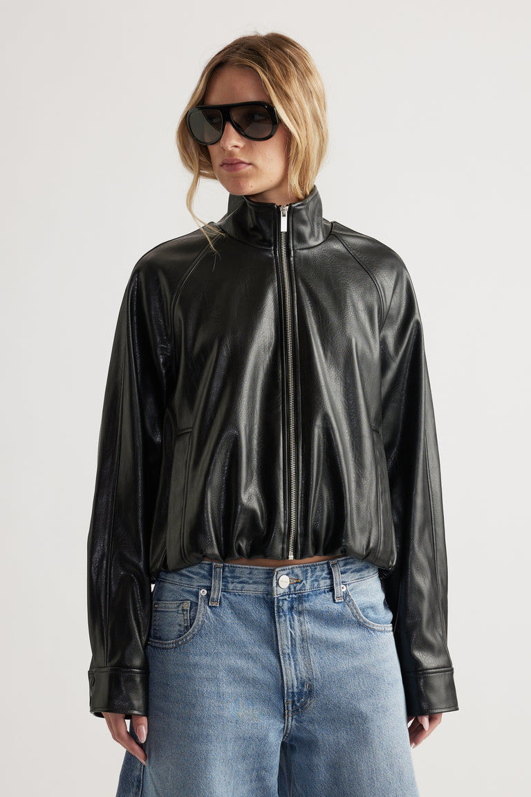 Woman wearing a relaxed fit black faux leather bomber jacket with high collar paired with light blue denim jeans