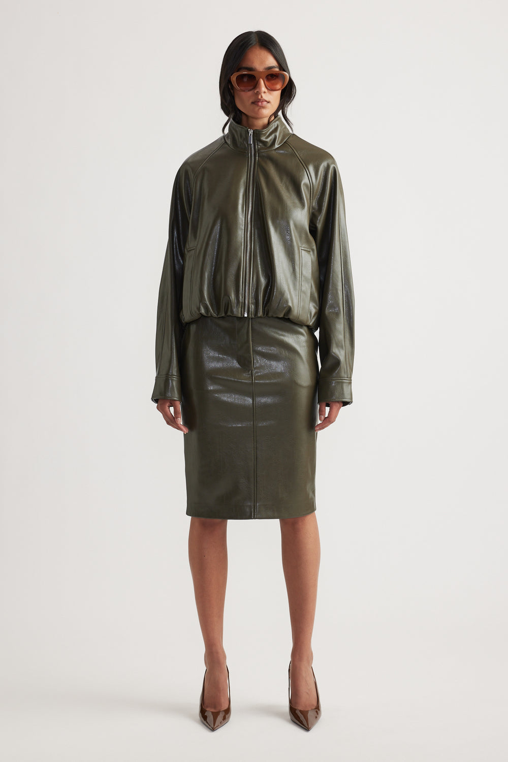 Woman wearing olive green faux leather bomber jacket with matching pencil skirt and brown pointed heels
