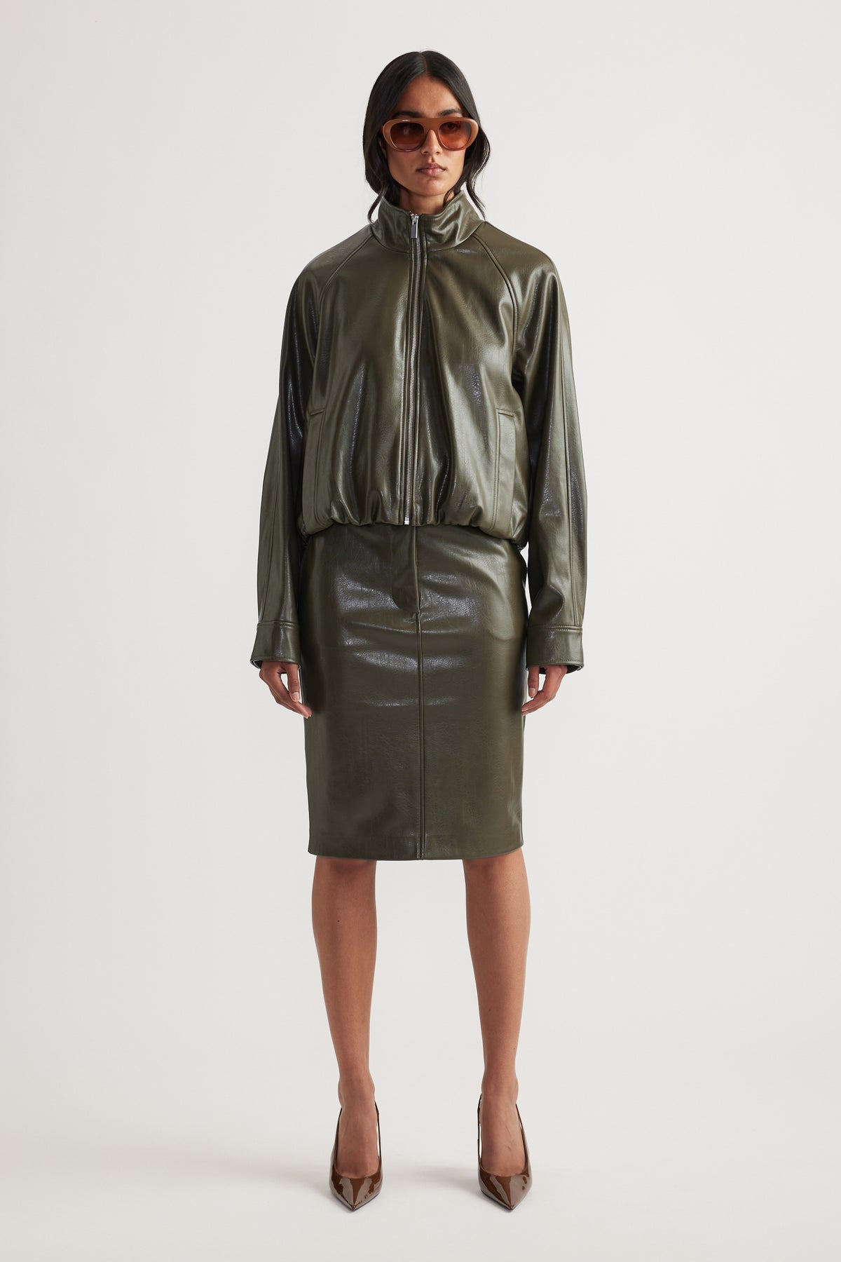 Woman wearing olive green faux leather bomber jacket with matching pencil skirt and brown pointed heels