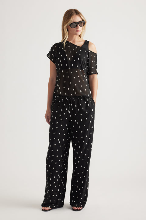 Woman wearing black wide-leg sheer pants with white spots paired with a matching sheer top and black sunglasses